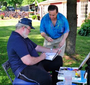 Paul Scarborough takes time from his painting to give an autograph to local writer Gene Pisasale during the plein air event at the Barn Shoppes.