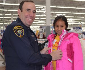 Deputy Sheriff Anthony Schuibbeo helps one of his young shoppers with a coat.